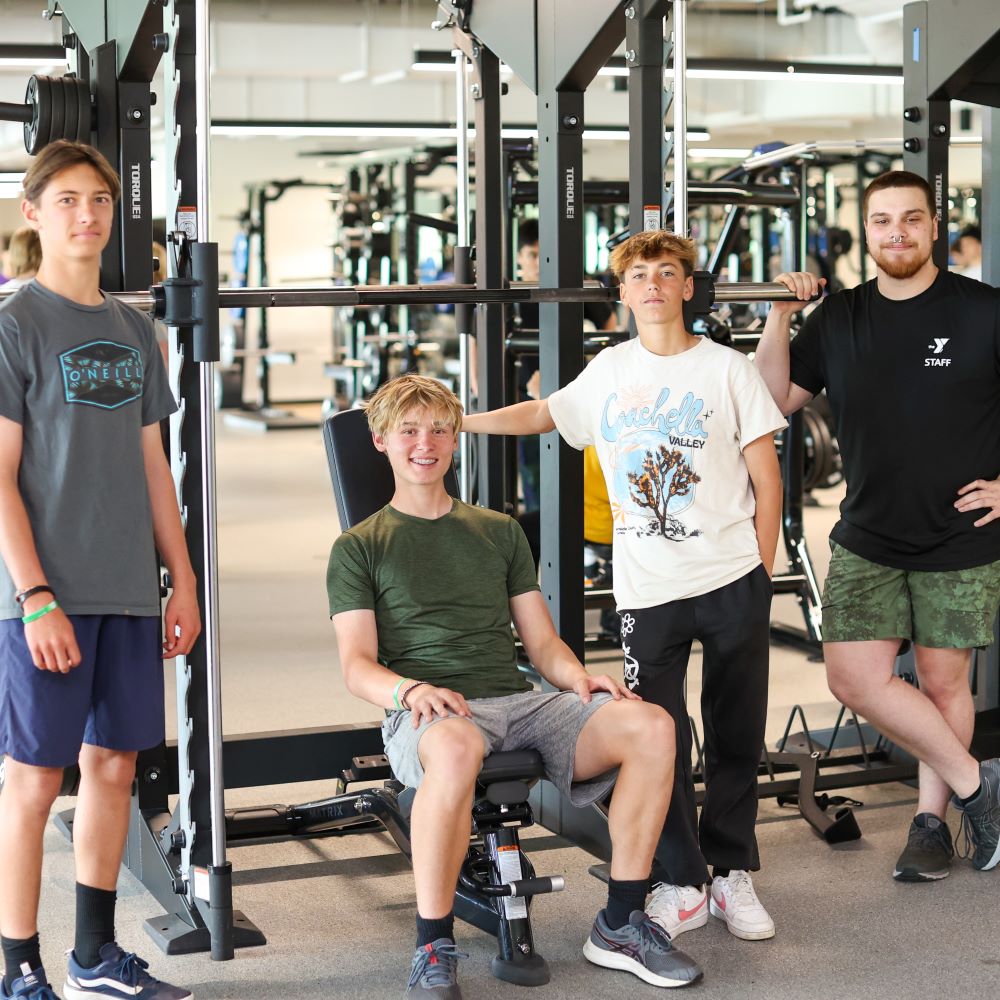 Three teens and a trainer pose by the Wellness Center's smith machine