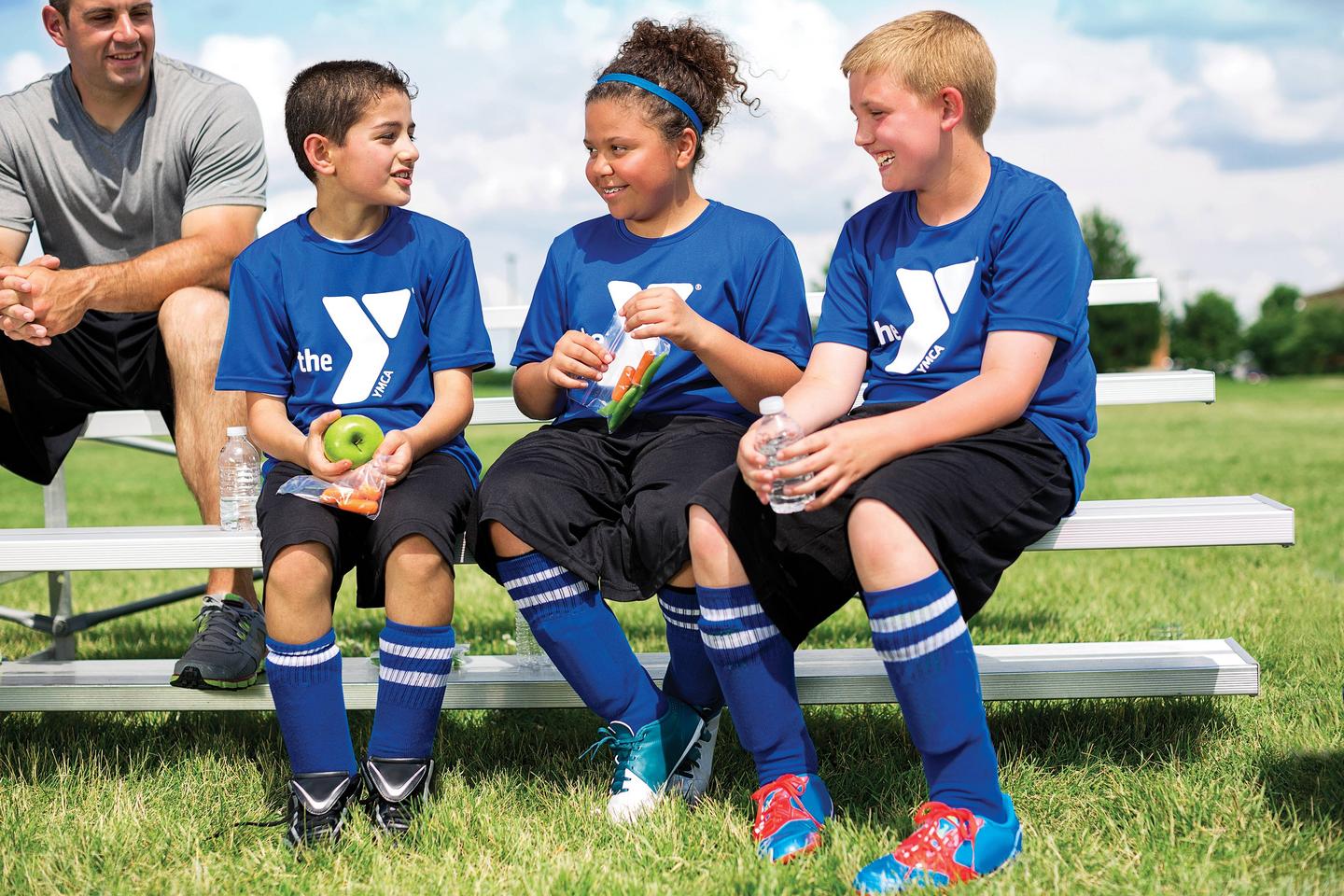 three youth in ymca soccer jerseys chatting on the sidelines