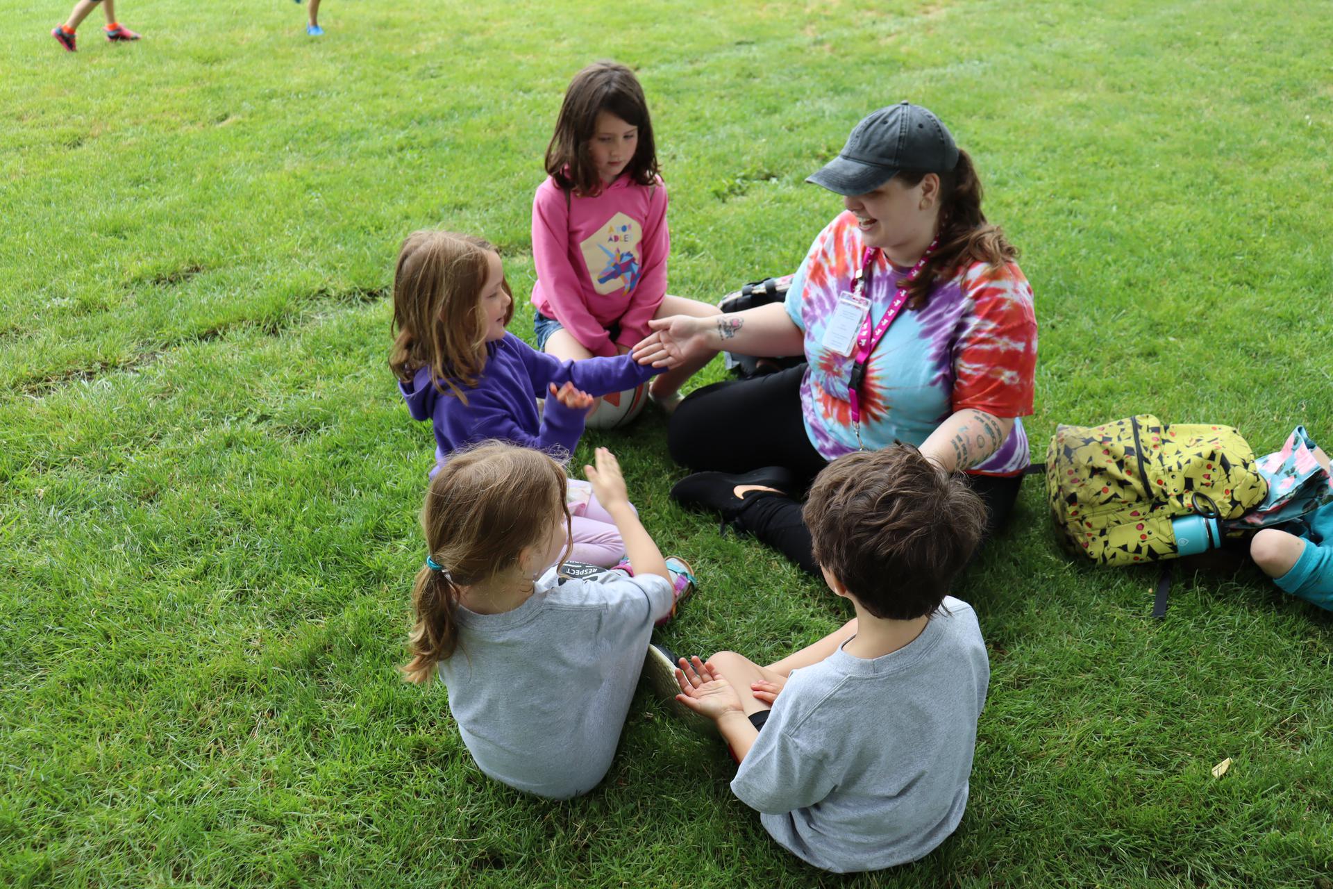 YMCA summer campers sit in a circle with a camp staff wearing tie dye